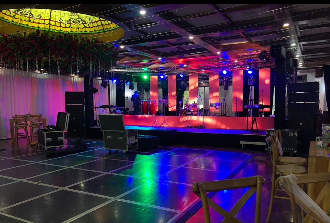 Salón con pista de baile iluminada, escenario y domo de vitral con flores